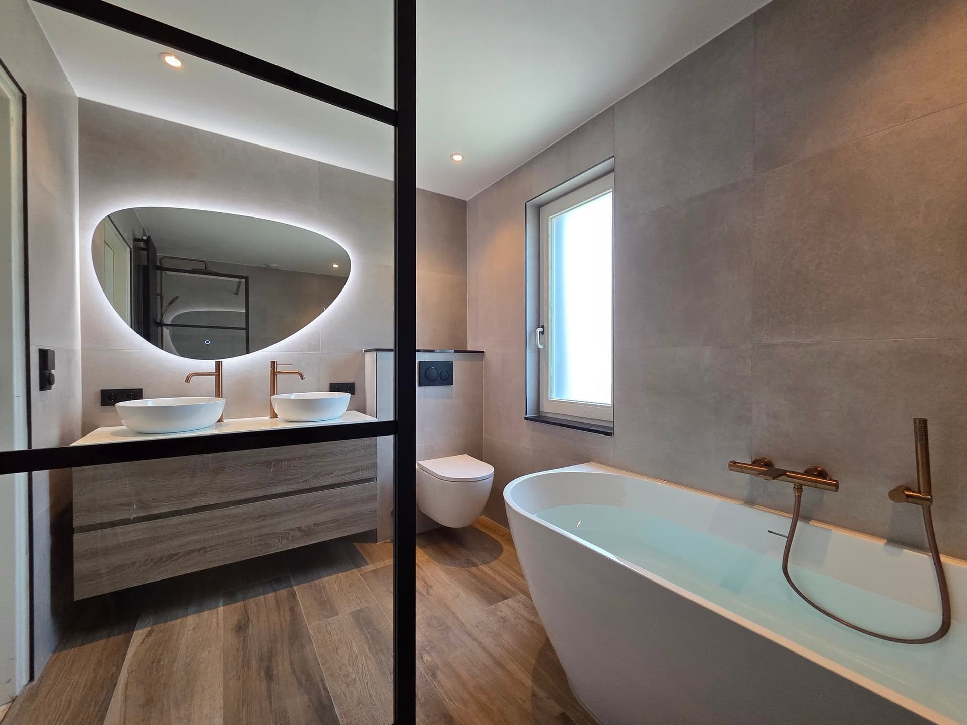 Badkamer met organische spiegel, dubbele wastafel en vrijstaand bad