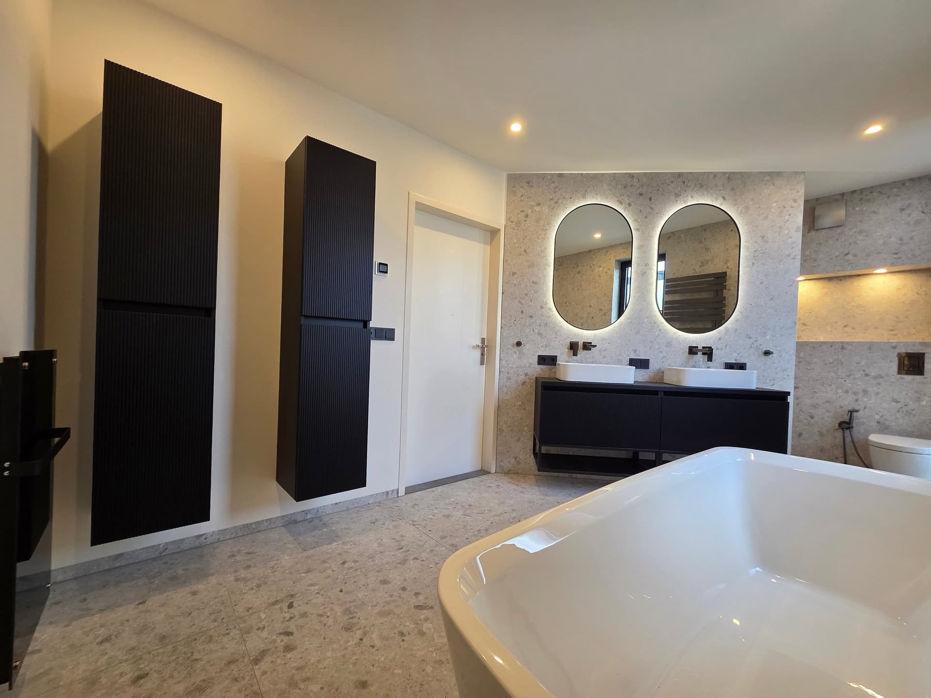 Badkamer met natuursteenlook, zwart wastafelmeubel en vrijstaand bad